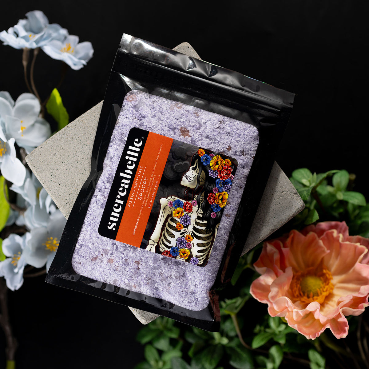 Sucreabeille Spoopy fizzing bath salt pouch with a colorful skeleton label, framed by flowers.